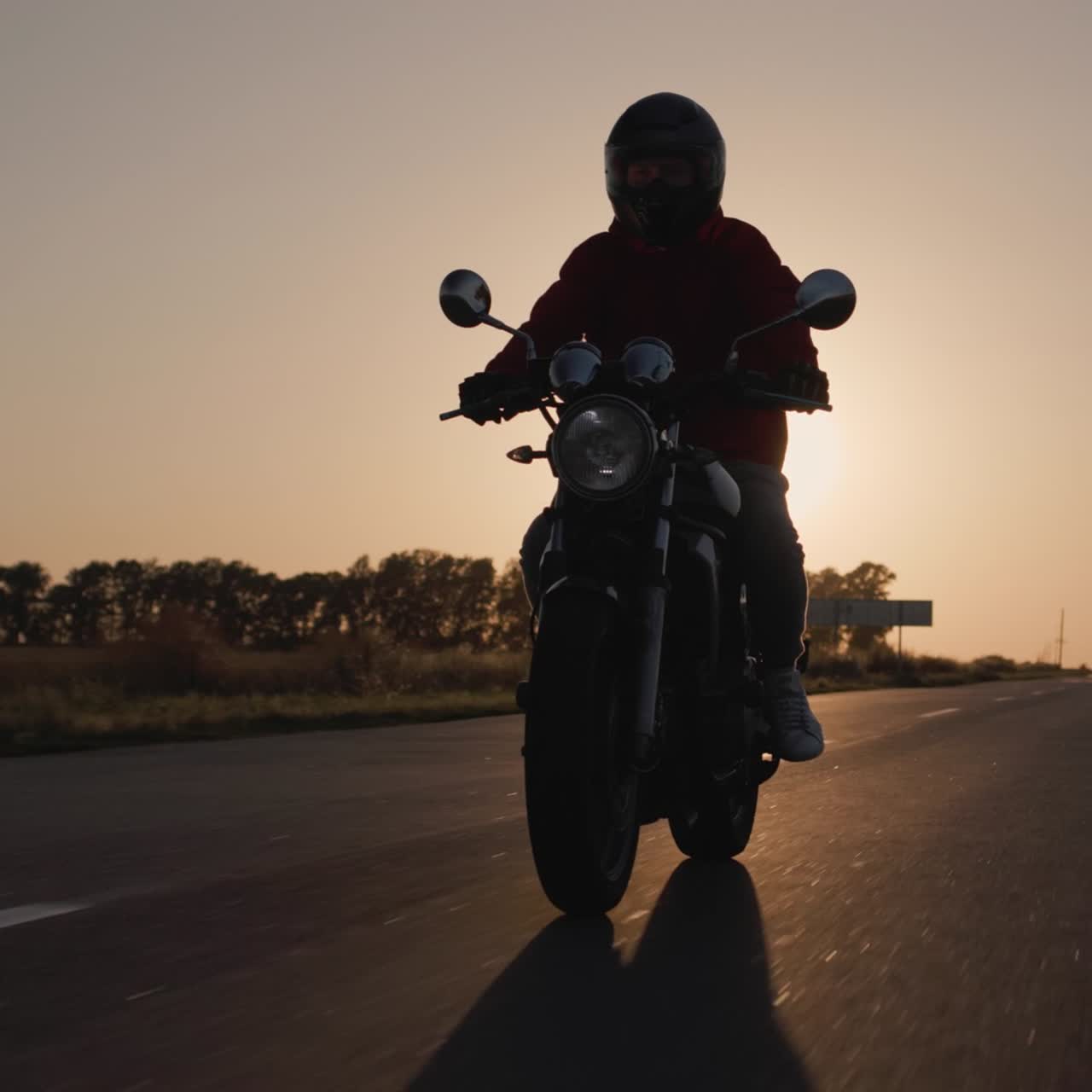 Silueta de un motorista en motocicleta circulando al atardecer por la autopista