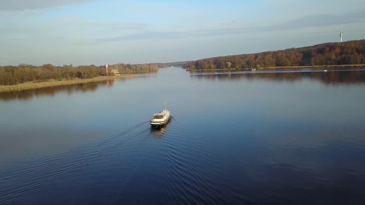 Ripresa con drone panoramica a destra di un battello passeggeri che avanza sul fiume Elba Labe, con riflessi d'acqua lisci e calda luce serale sugli alberi autunnali.