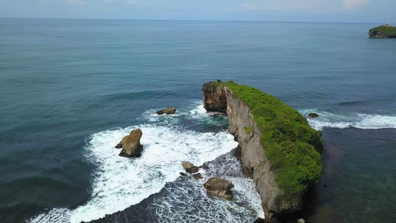 파도에 부서지는 작은 바위들이 모여 있는 거대한 산호 바위가 있는 열대 해변의 드론 보기