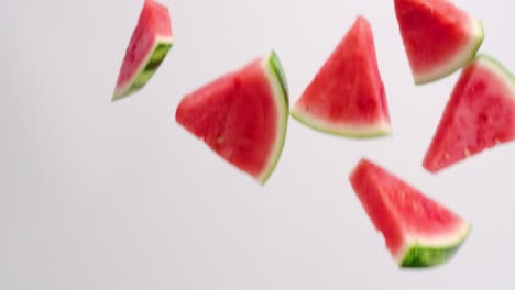 cuñas cortadas de sandía rosa brillante y fresca con corteza verde lloviendo sobre fondo blanco en cámara lenta