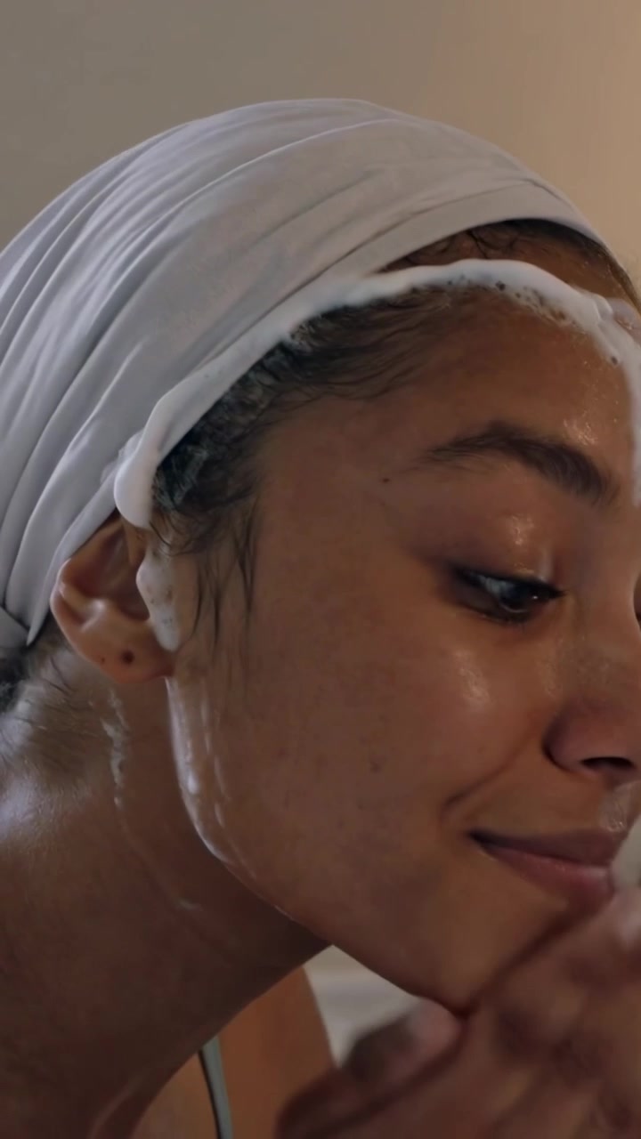 Vertical video: Applying foam, woman massaging face at bathroom sink, removing makeup in towel