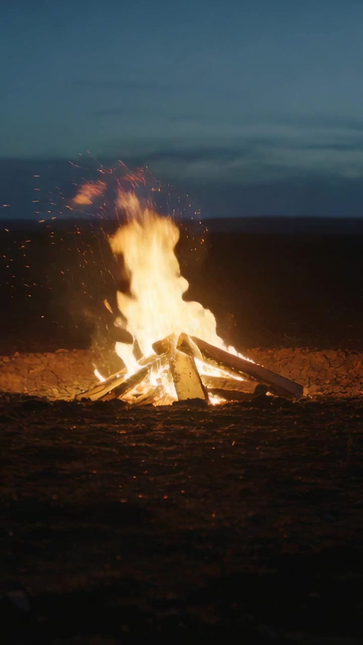 Video vertical: Encendiendo tablones y troncos de madera apilados ardiendo más alto al anochecer, consumiendo la madera.