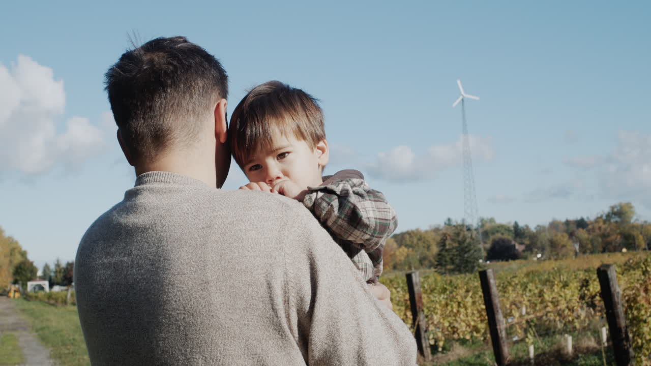 un agricultor con un hijo pequeño en sus brazos se encuentra contra el fondo de un viñedo