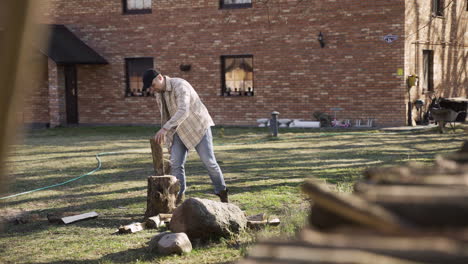 Distant-view-of-caucasian-man-chopping-firewood-with-an-ax-outside-a-country-house