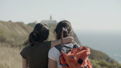 Rückansicht-Von-Zwei-Kaukasischen-Mädchen-Im-Teenageralter,-Die-An-Einer-Klippe-Stehen-Und-Den-Meerblick-Bewundern