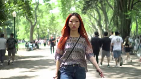in a vibrant park filled with people enjoying the outdoors, a young woman strides with confidence, showcasing her style and presence amidst the lively atmosphere.