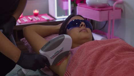 una mujer joven en un spa recibe tratamiento de depilación con láser en sus axilas