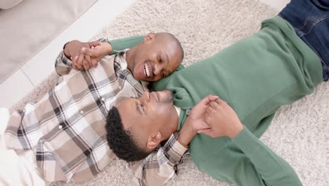 Happy-african-american-gay-male-couple-lying-on-floor,-embracing-and-smiling,-slow-motion