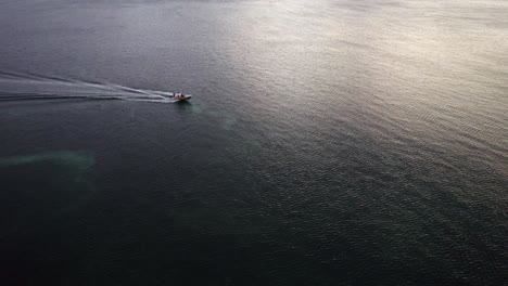 Barco-Motorizado-Deslizándose-Por-El-Océano-Azul,-Mientras-El-Reflejo-Del-Atardecer-Golpea-El-Agua-En-Roatán,-Honduras