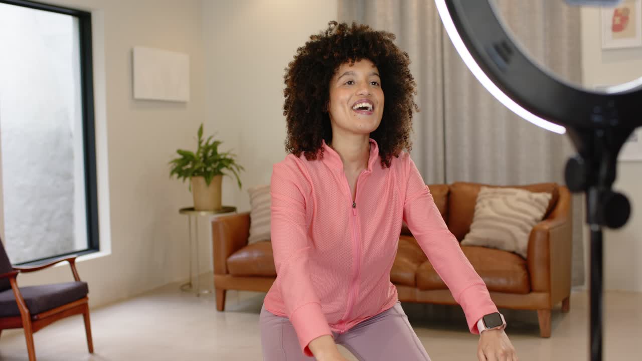 Allenatrice afroamericana con ring light che mostra squat su un tappetino viola in soggiorno