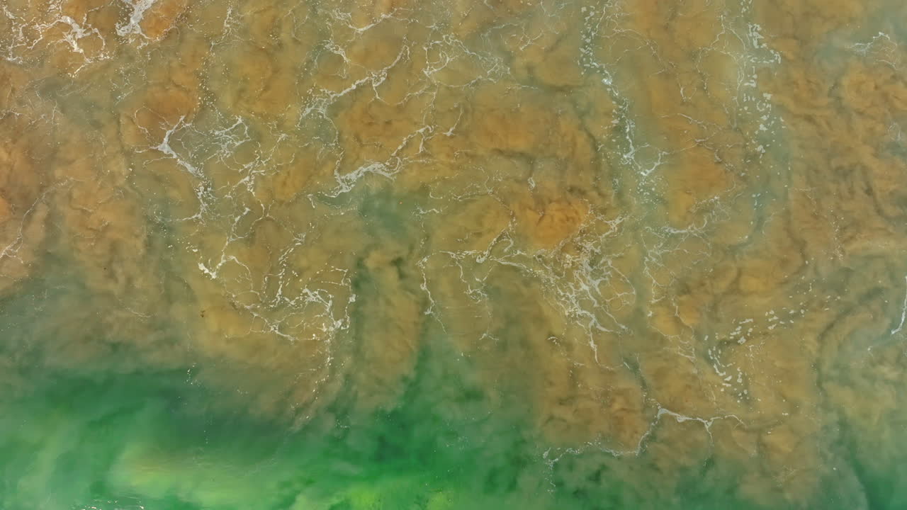 Waves with risen sand from a bottom splashes onto the shore. Coastline of the Pacific Ocean from aerial perspective.