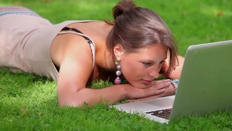 smiling student lying on grass looking at laptop