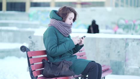 woman using phone on a park bench in winter