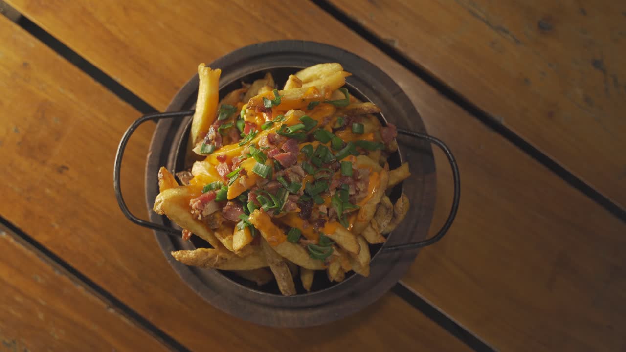 primer plano de un recipiente giratorio con patatas fritas o patatas fritas y queso cheddar, tocino y cebolla verde