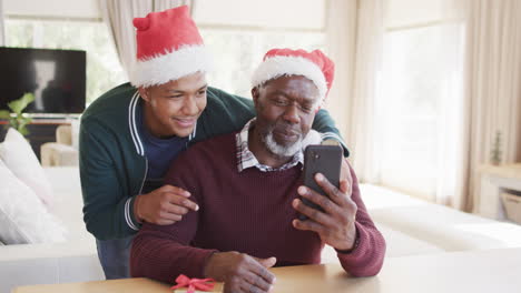 Happy-african-american-father-and-son-in-christmas-hats-having-smartphone-video-call,-slow-motion