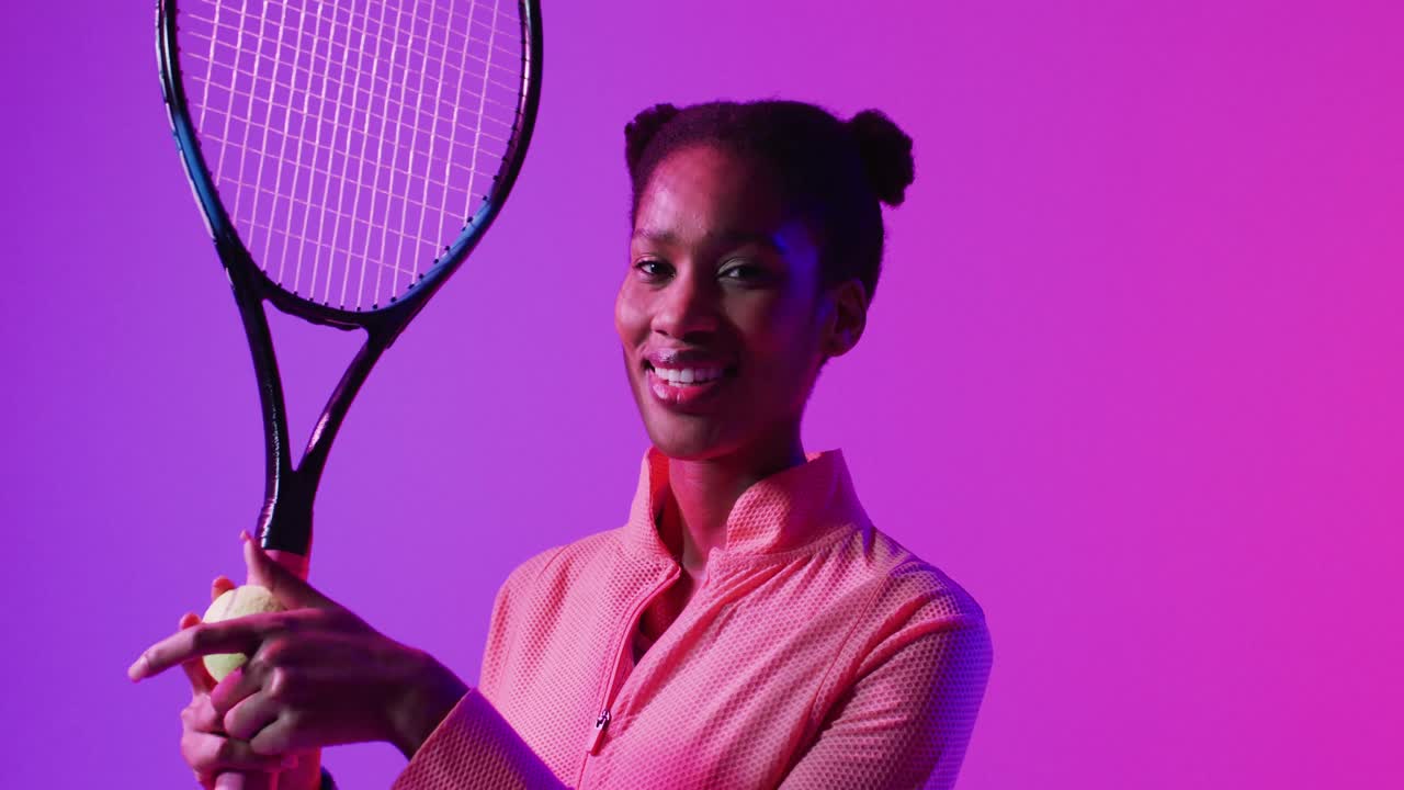Video of happy african american female tennis player with racket in neon pink lightning