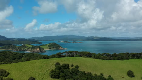 Vista-Aérea-De-La-Pintoresca-Bahía-De-Islas-Aera,-Nueva-Zelanda,-Drone-Que-Revela-Una-Toma-De-Exuberantes-Colinas-Con-Palmeras-Y-El-Océano-Azul-En-El-Fondo