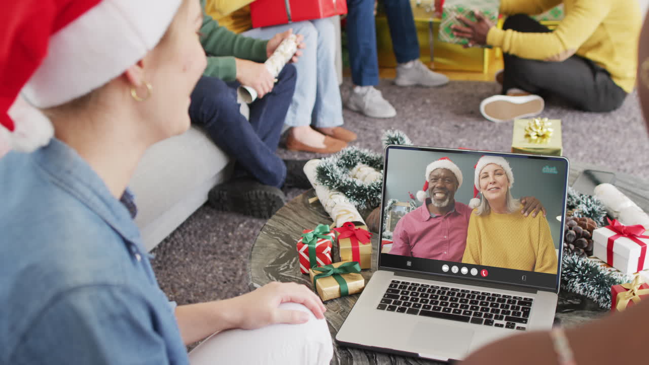 Animation of diverse friends in santa hats on laptop video call with couple at christmas