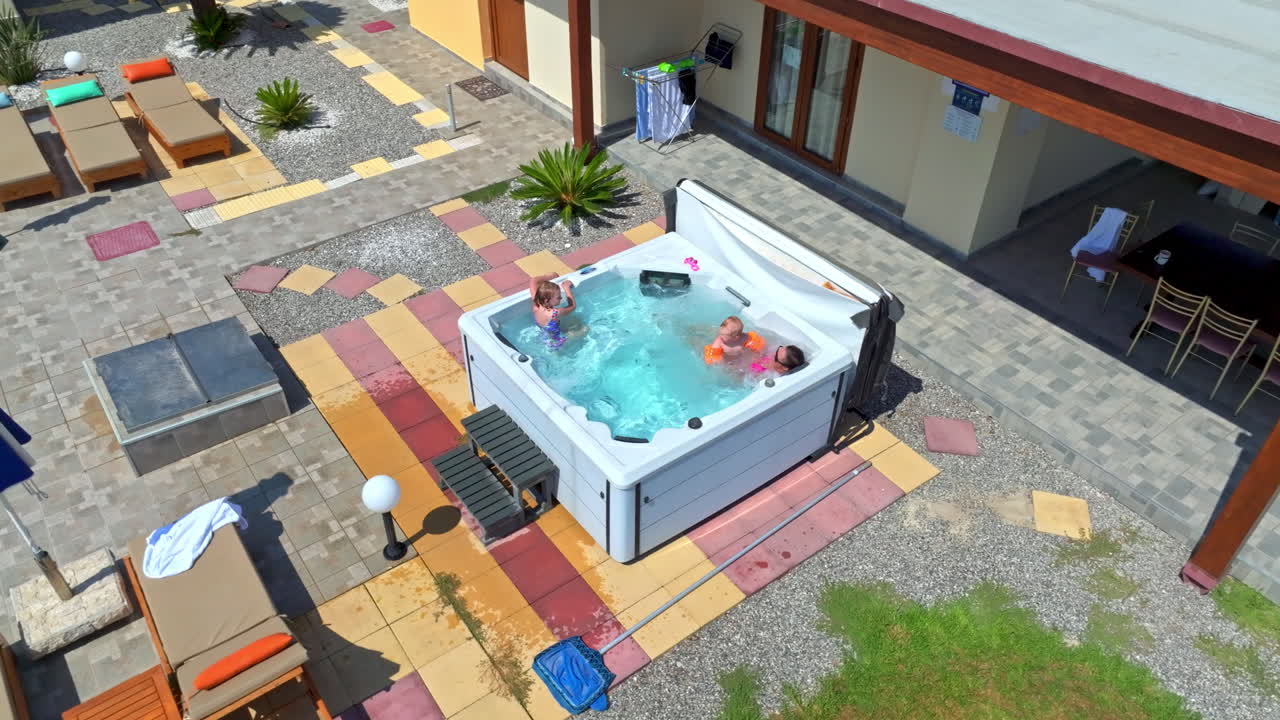 Aerial view orbiting a mother and children relaxing in a jacuzzi, sunny day