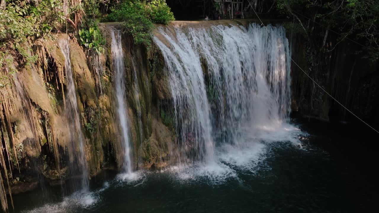 Drone captures stunning close aerial of jungle waterfall plunging over mossy rock into deep dark water in remote Guatemala.