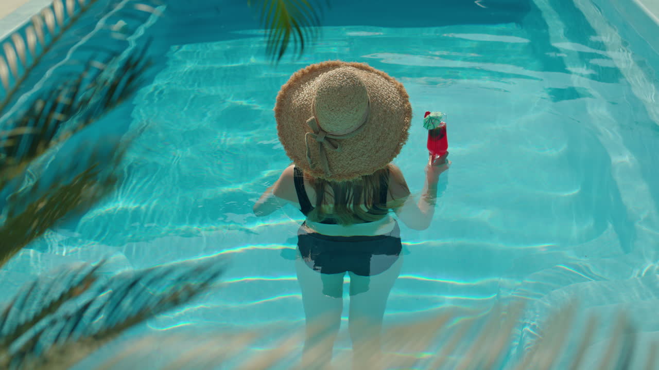 Woman in a straw hat enjoying a cocktail in a swimming pool