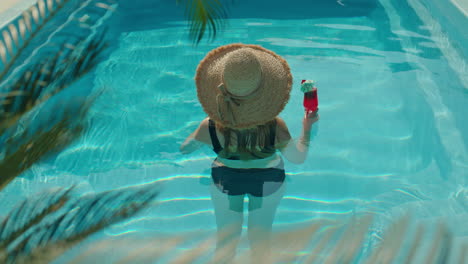 woman in a straw hat enjoying a cocktail in a swimming pool