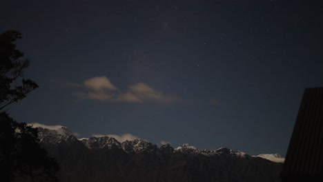 a serene night sky with stars and clouds over snow-capped mountains in queenstown, new zealand. captured with steady camera and soft lighting