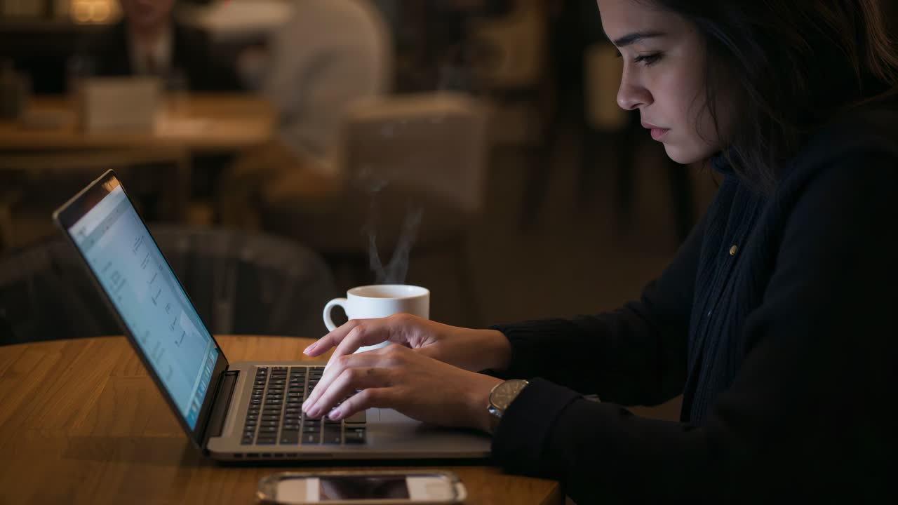 Settling woman in dark jacket typing on laptop, finishing work in cafe, mug steaming, copy space