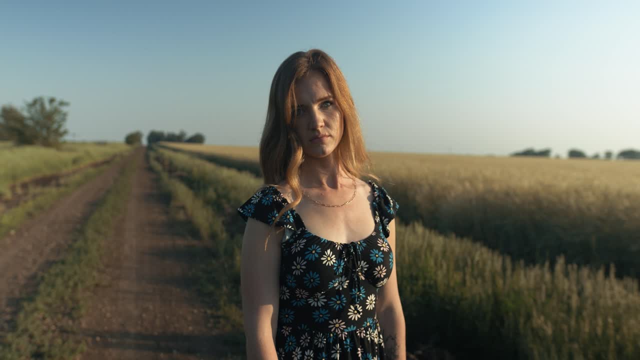 Young woman on dirty country, road enjoying the calm, peaceful and serene summer sunset with light shining on her hair during golden hour in cinematic slow motion