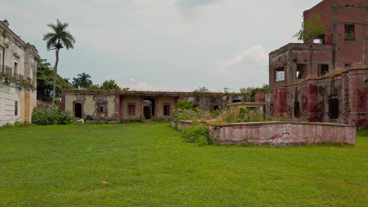 Rovine di un'hacienda storica con cortile invaso dalla vegetazione, edifici logori, palme, erba e muri fatiscenti a Morelos, Messico, che mostrano architettura coloniale abbandonata e degrado.