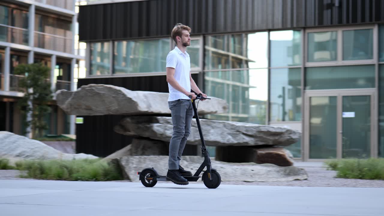 Businessman rides past modern building on his e-scooter, wide shot