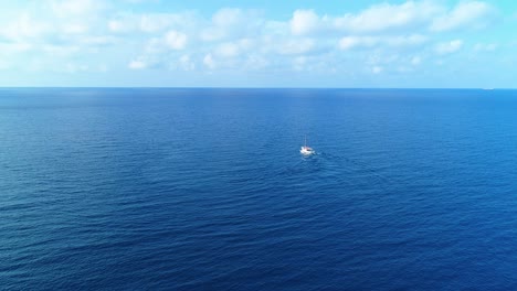 Sailboat-turns-out-to-sea-on-voyage-into-cloudy-horizon,-aerial-static