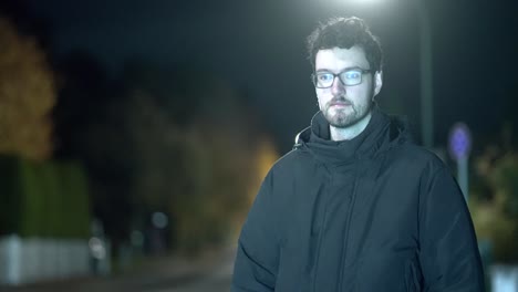 Young-Man-Stands-Alone-in-Chilly-Munich-Suburb-During-Frosty-Winter-Night,-Street-and-Car-Lights-Create-Vivid-Illumination