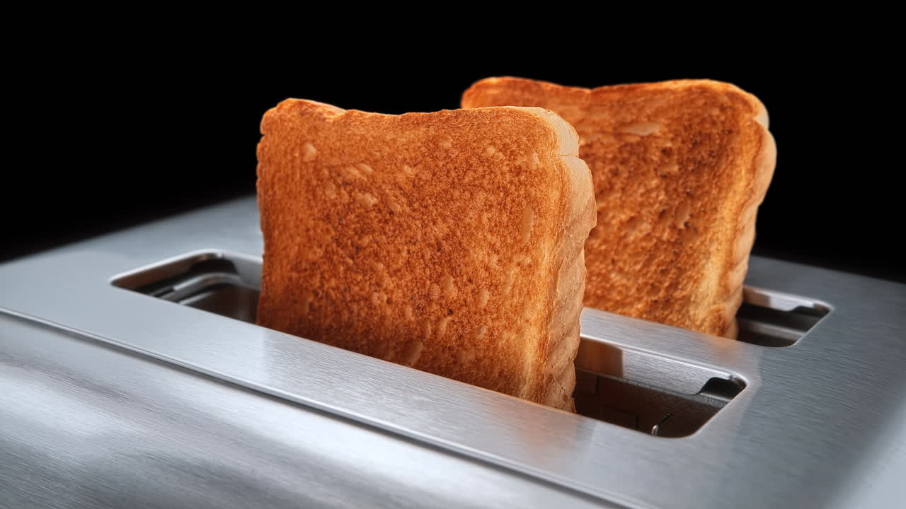 갈색 토스트 된  조각이 은 토스터 슬롯의 안쪽에서 느린 움직임으로 뛰어나옵니다.