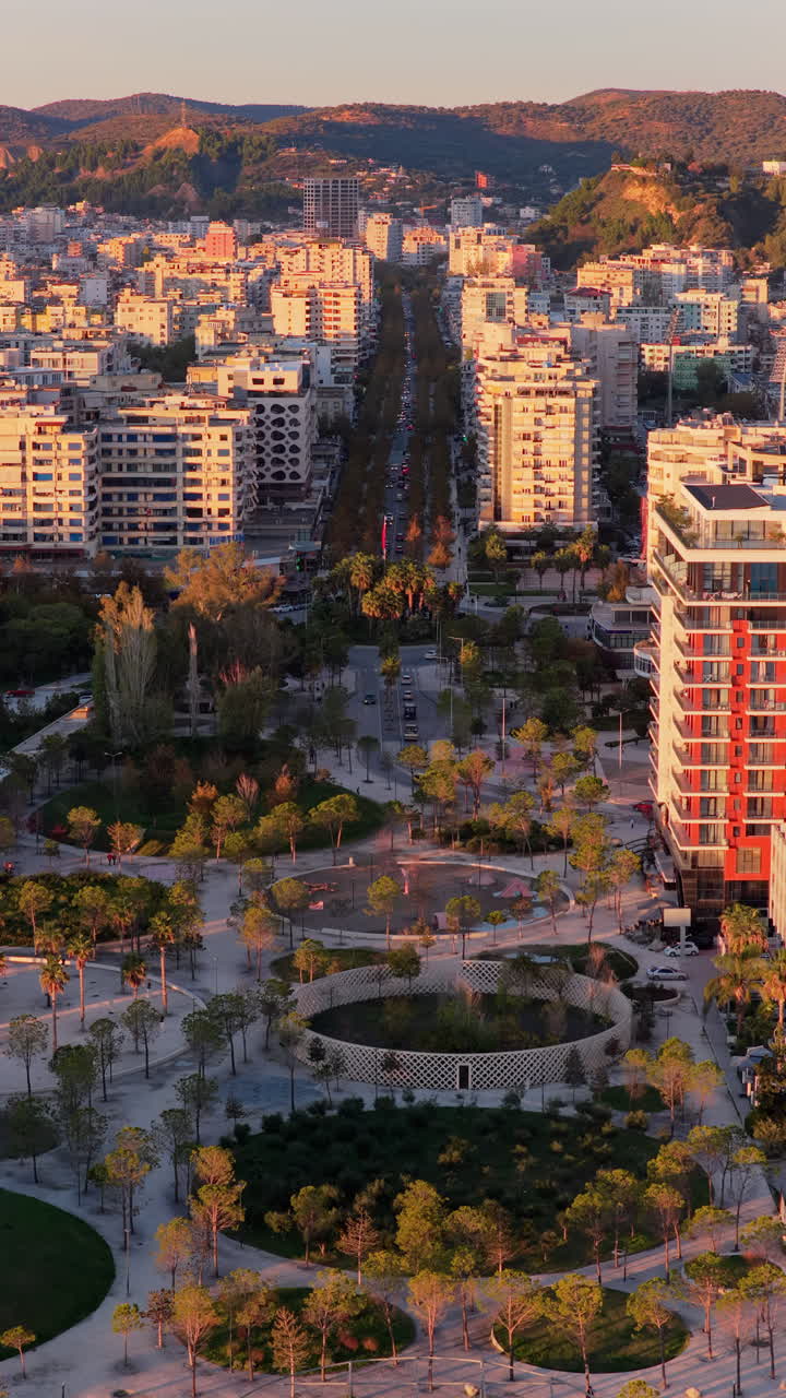 Aerial drone view of the golden hour lighting highlighting Vlora's central urban park, featuring circular pathways, palm trees, playgrounds, and landscaped green spaces. Durres, Albania, Vertical
