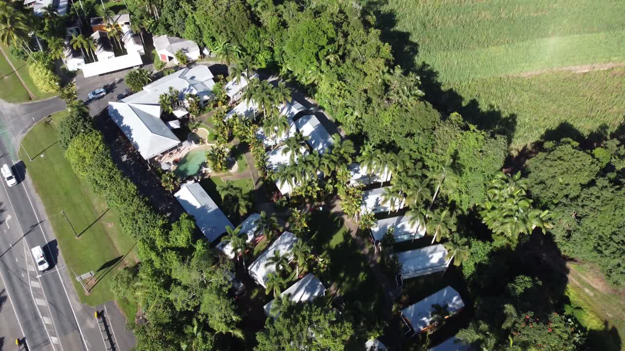 4K Aerial view of a small holiday resort with individual villas and a swimming pool near a sugarcane plantation in North Queensland, Australia
