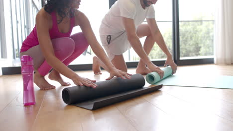 biracial couple rolling yoga mats at home, in slow motion