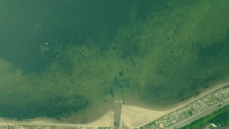 Top-down-aerial-shot-narrow-coastline-close-to-the-sea,-rocky-shore-and-descent-into-the-sea