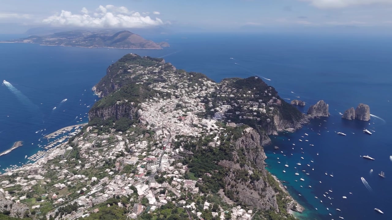 Ripresa con drone dell'isola di Capri, che ne evidenzia l'immensa bellezza naturale con vegetazione lussureggiante, scogliere e acque blu.
