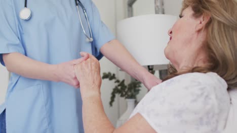trabajadora de la salud que sostiene las manos de una mujer mayor en casa.