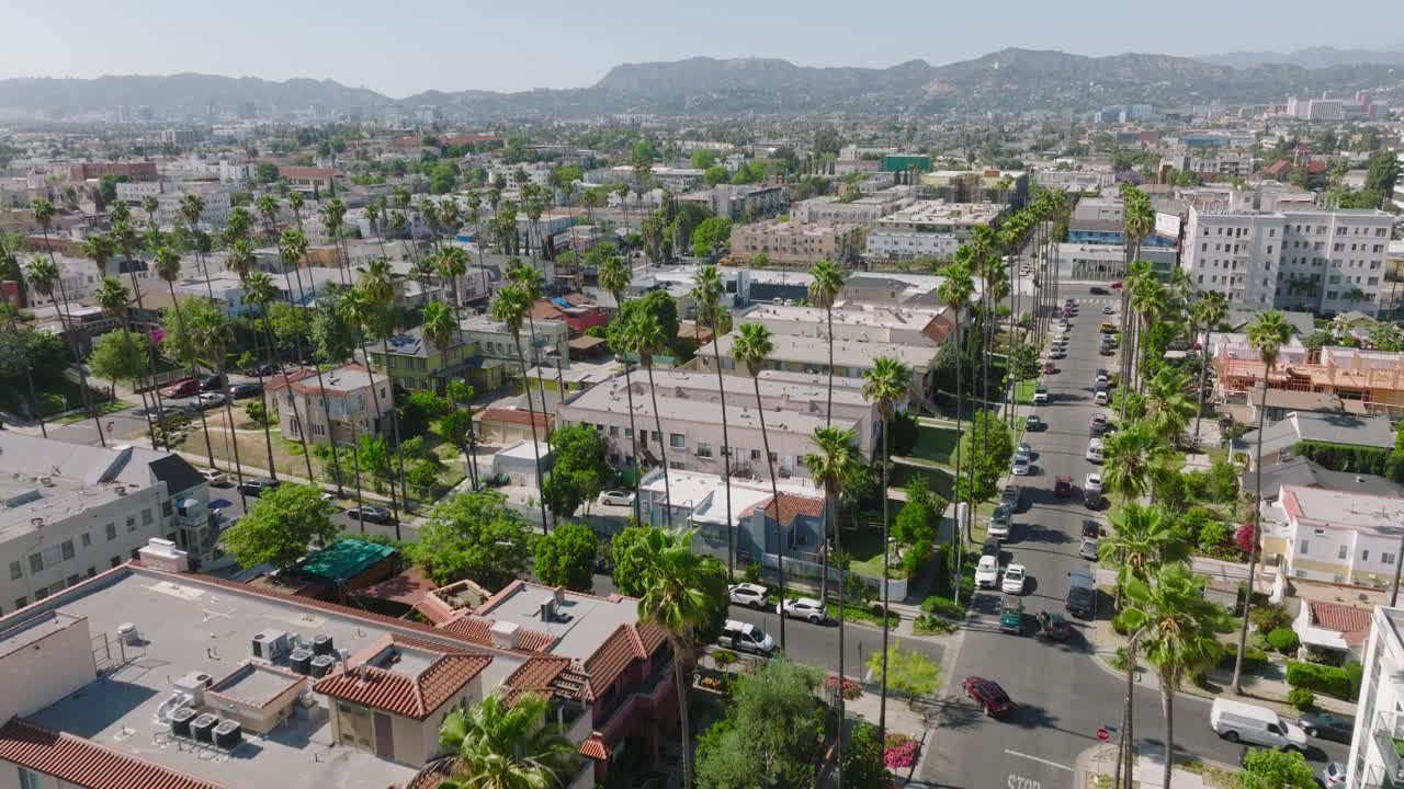 아래에 야자수가 늘어선 거리와 지평선 배경에 산이 있는 로스앤젤레스 아파트 상공에서 공중 드론이 촬영되었습니다.