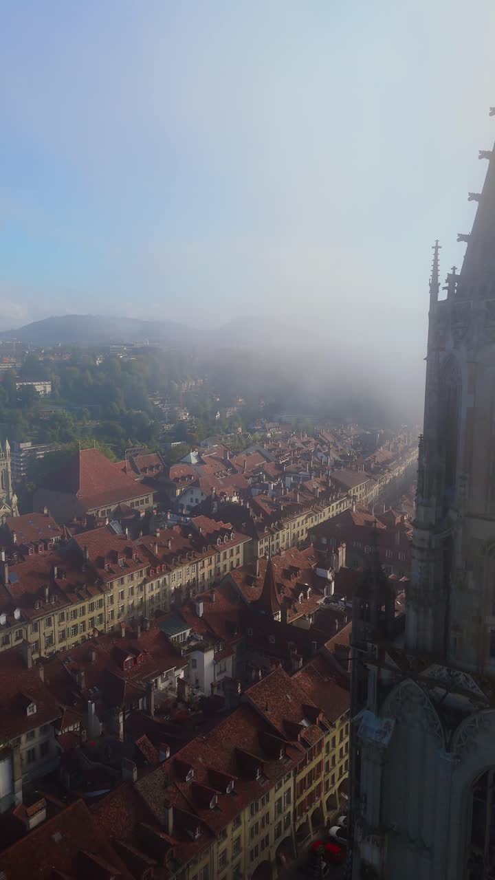 Volo di drone sopra la città vecchia di Berna durante nebbia e alba, passando vicino alla Cattedrale di Münster.