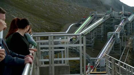 people observe an illuminated futuristic industrial structure in a mountain landscape