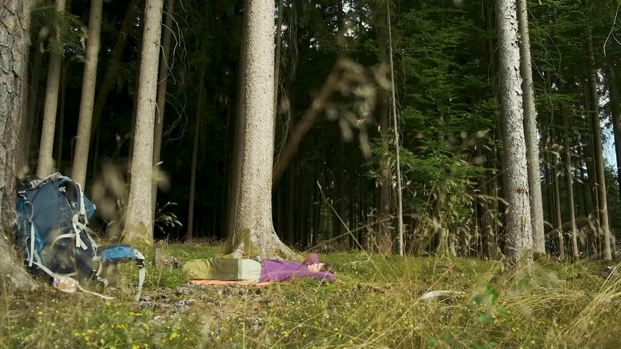 A woman sleeps peacefully in a sun-dappled forest clearing during a solo hike. This tranquil shot is perfect for themes of relaxation, wellness, and connecting with nature