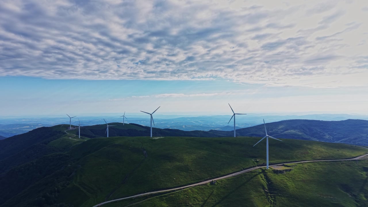 Wind turbines stand on the hill under a cloudy sky in the morning