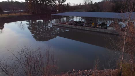 Drone-footage-going-up-from-the-ground-to-the-sky-with-land-and-lake-in-foreground-and-boats-and-boat-dock-in-background-during-sunset