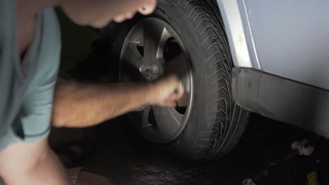 replacing car tire at night tightening nuts with angled wrench