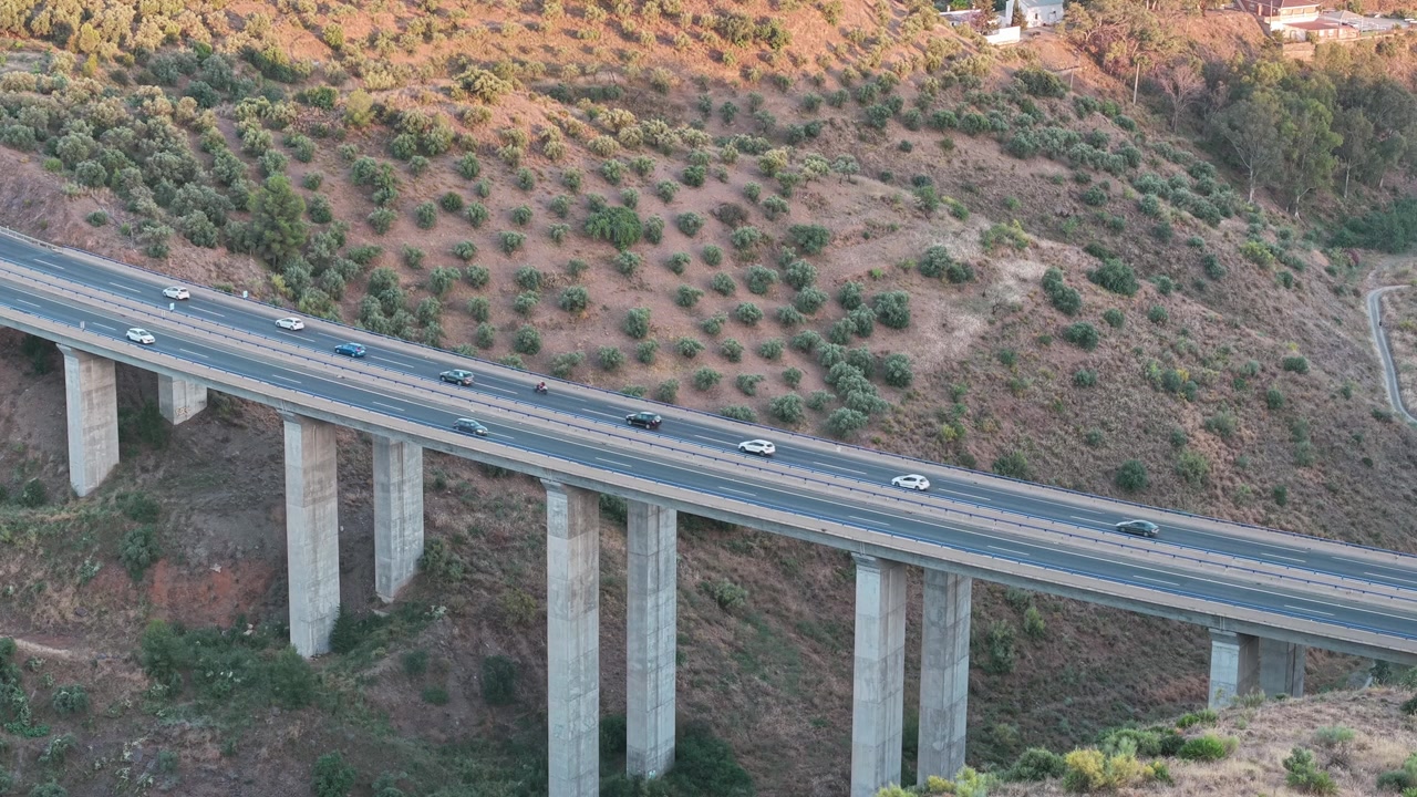 Auto che attraversano un alto viadotto in cemento che si estende su un terreno collinare arido a Malaga, Spagna