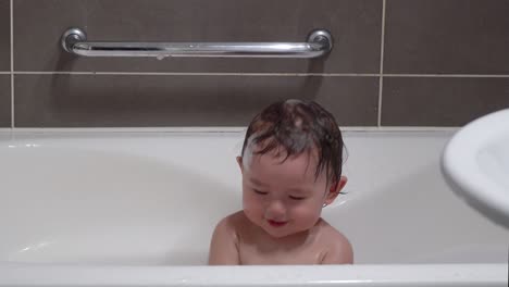 adorable asian toddler clapping hands while bathing in a baby bathtub in the bathroom