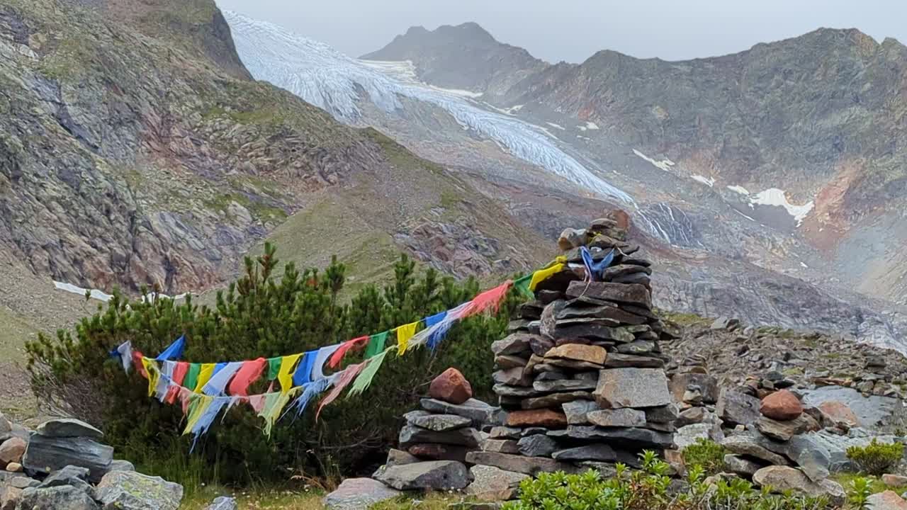 amplia vista de banderas de oración nepalesas desgastadas en el viento frente a piedras y arbustos y un glaciar remoto